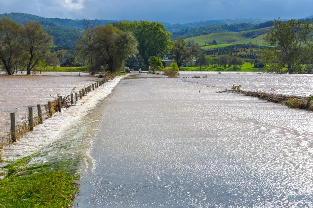 Flooded rural farmland with damaged fence and overflowing water, highlighting flood prevention issues.